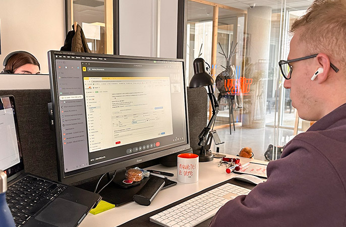 Sylvain de Tizy configure un projet client sur son ordinateur, concentré devant son écran dans un open space moderne.