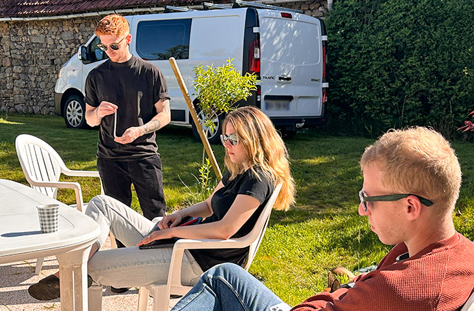 Séminaire Tizy – Moment d’échange au soleil Trois membres de l’équipe Tizy échangent en extérieur durant un séminaire, assis autour d’une table dans un jardin ensoleillé.